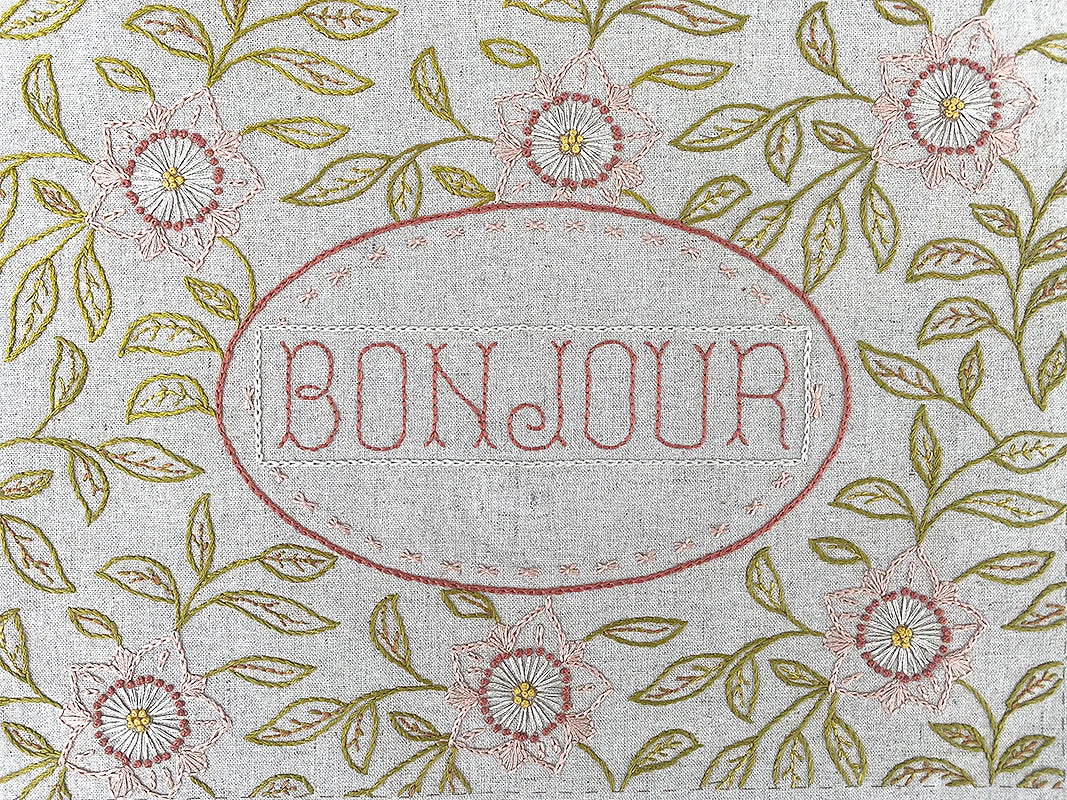 Linen sampler with 'Bonjour' embroidery surrounded by floral and leaf patterns