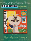 A quilted wall hanging featuring a whimsical design with a cat, keyboard, and other objects, with a red, orange, and white color scheme.