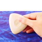 Up close view of a hand holding a off-white tailor chalk on a blue fabric background