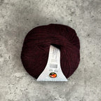 A ball of burgundy yarn with a white paper label, placed on a textured gray concrete surface.