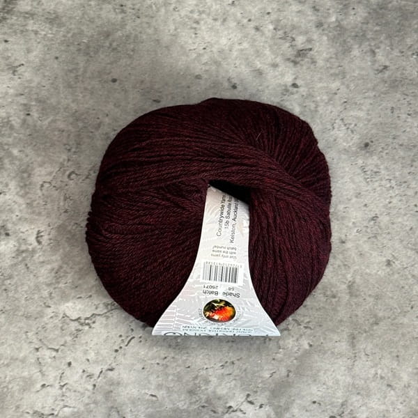 A ball of burgundy yarn with a white paper label, placed on a textured gray concrete surface.