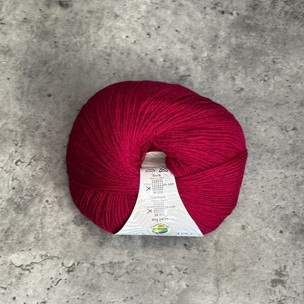 A ball of vibrant Fuchsia yarn with a white paper label, placed on a textured gray concrete surface.
