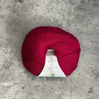 A ball of vibrant Fuchsia yarn with a white paper label, placed on a textured gray concrete surface.