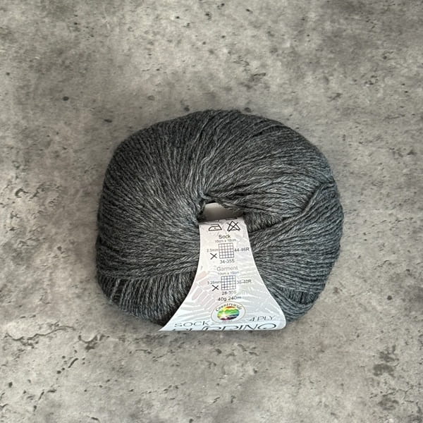 A ball of grey marl yarn with a white paper label, placed on a textured gray concrete surface.