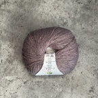 A ball of lavender-grey yarn with a white paper label, placed on a textured gray concrete surface.