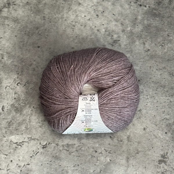 A ball of lavender-grey yarn with a white paper label, placed on a textured gray concrete surface.
