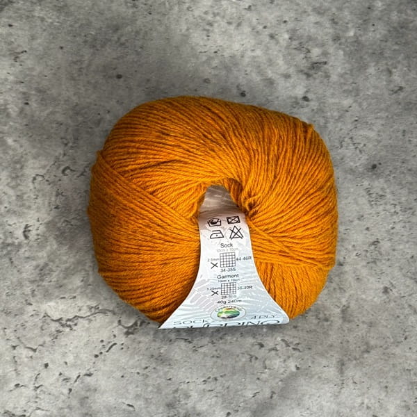 A ball of mustard yarn with a white paper label, placed on a textured gray concrete surface.