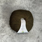 A ball of olive green yarn with a white paper label, placed on a textured gray concrete surface.