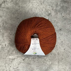 A ball of deep rusty brown yarn with a white paper label, placed on a textured gray concrete surface.