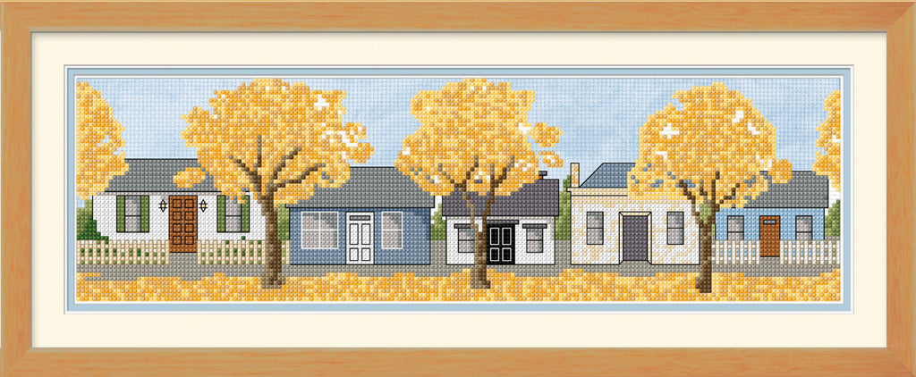 Cross-stitched scene of Arrowtown  row of houses with yellow trees in front, framed in wood.