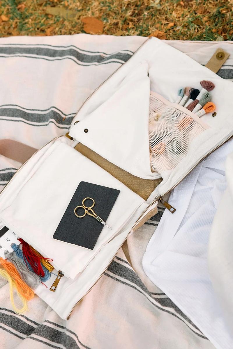 Open white craft bag with craft supplies  other items on a striped fabric background