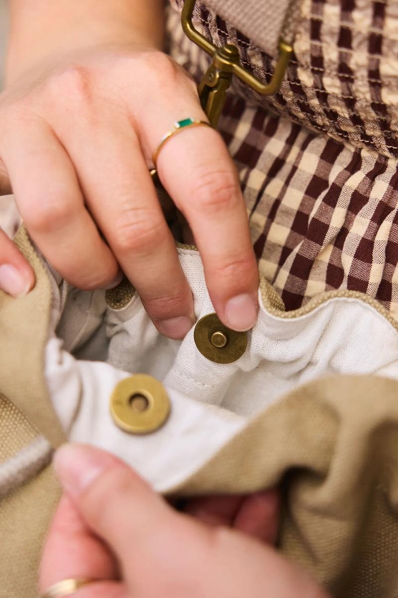 Close-up of hands buttoning a craft storage bag with brass snap.
