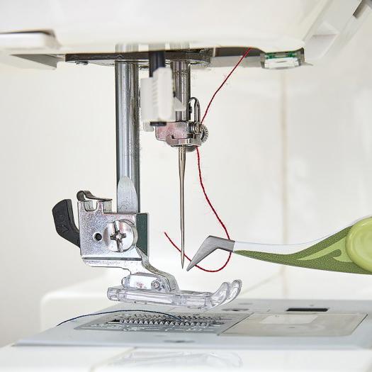 Close-up of a sewing machine needle and presser foot with a fabric tweezer in use 