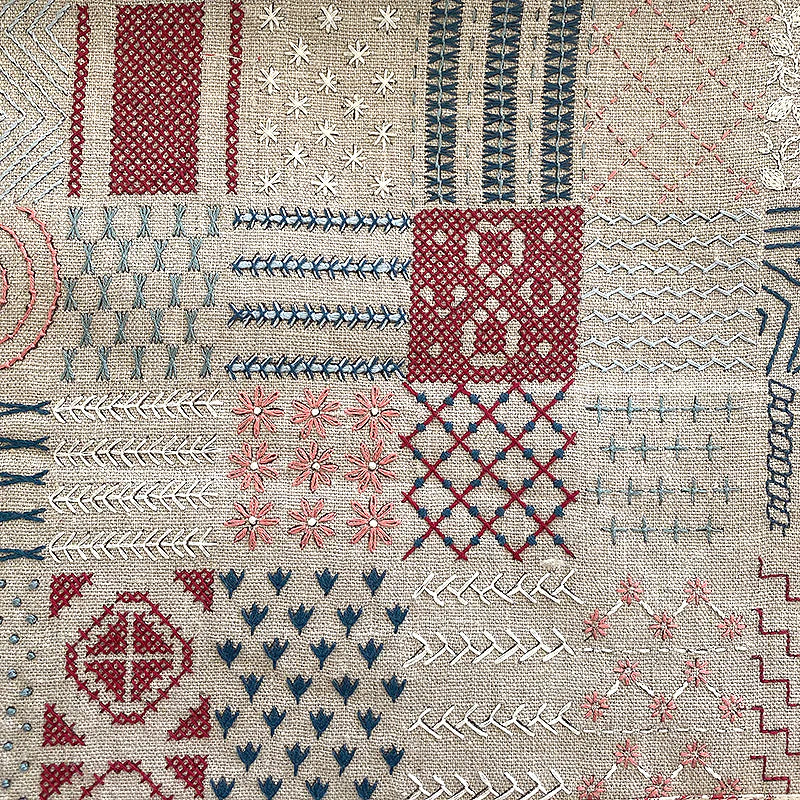 Example of complete French General sampler with various embroidered patterns in red, blue, and white on a beige background.