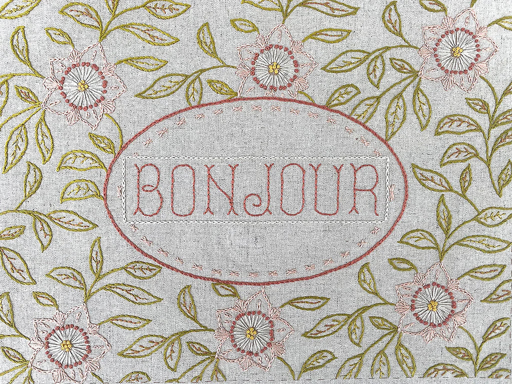 Linen sampler with 'Bonjour' embroidery surrounded by floral and leaf patterns