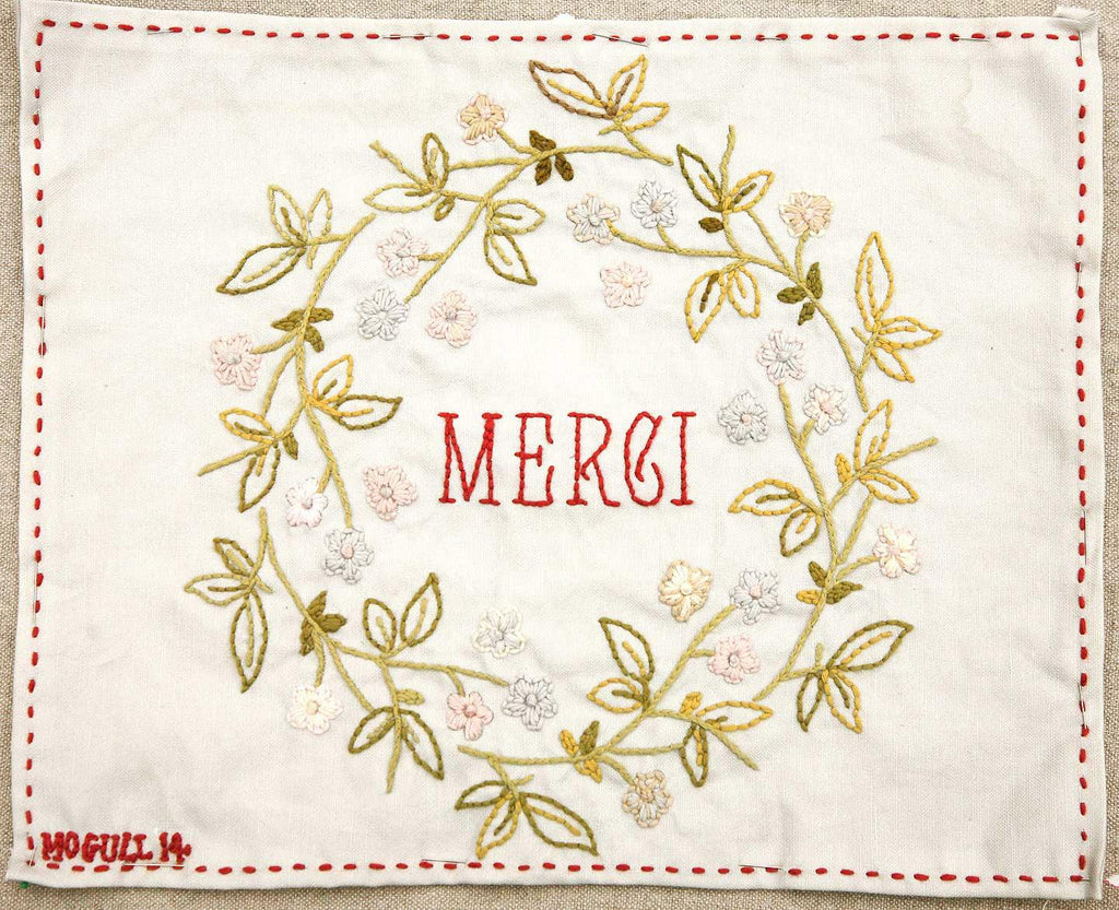 Embroidered fabric with floral wreath and 'MERCI' text on a off-white background