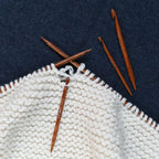 Knitting needles and a partially knitted white fabric on a dark blue background