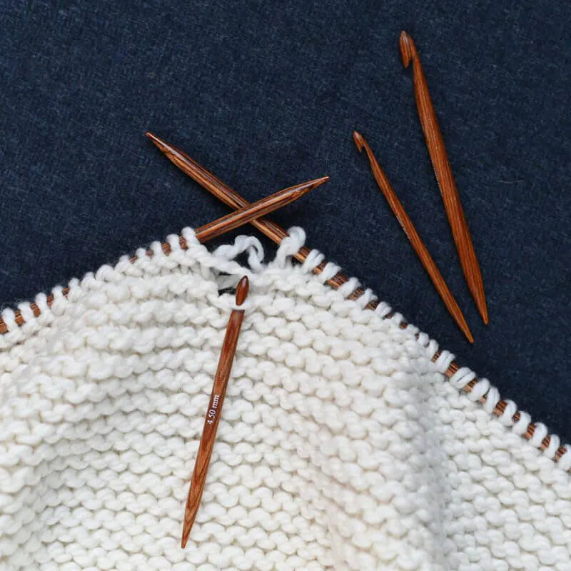 Knitting needles and a partially knitted white fabric on a dark blue background