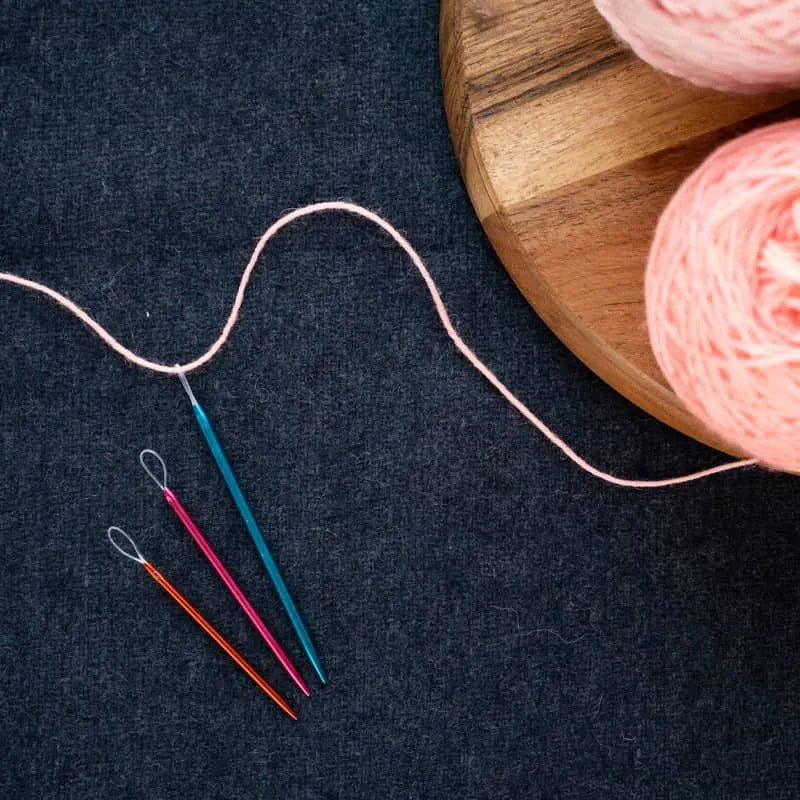 Pink yarn with sewing up needles on a dark surface
