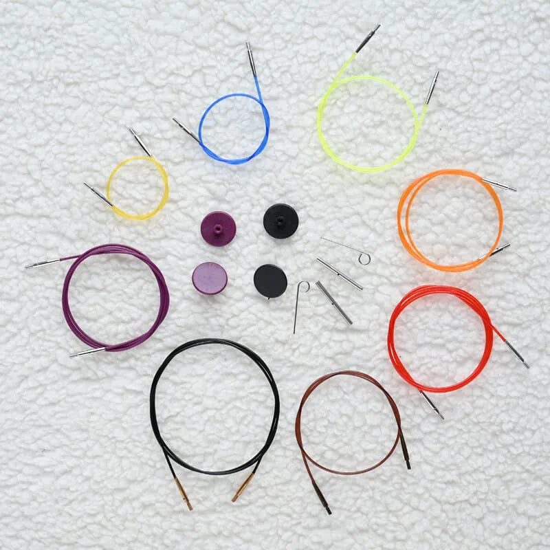 Set of colorful circular knitting needle cables and accessories on a textured white background