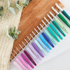 Set of colorful crochet hooks on a wooden board with a crocheted item and leaves in the background.