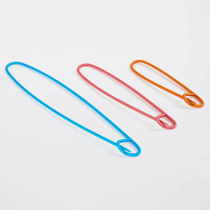Three colorful stitch holders for  knitters (blue, red, orange) on a light gray background.