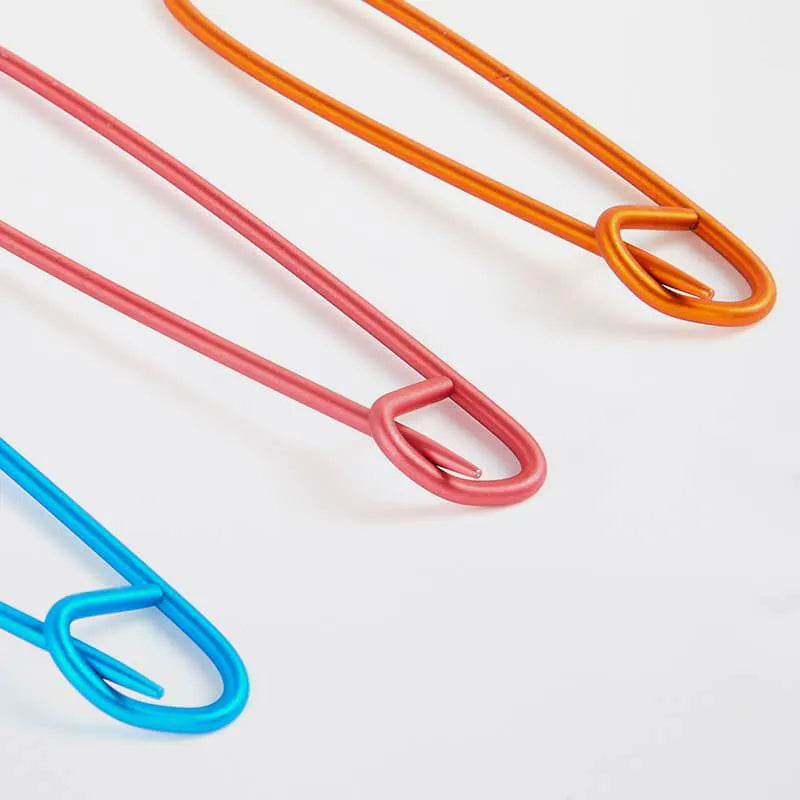 Close up of three colorful stitch holders for  knitters (blue, red, orange) on a light gray background.