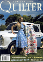 Magazine cover featuring a woman holding a quilt next to a vintage car in a scenic setting.