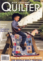 Magazine cover featuring a child playing guitar on a quilt with text about New Zealand Quilter.