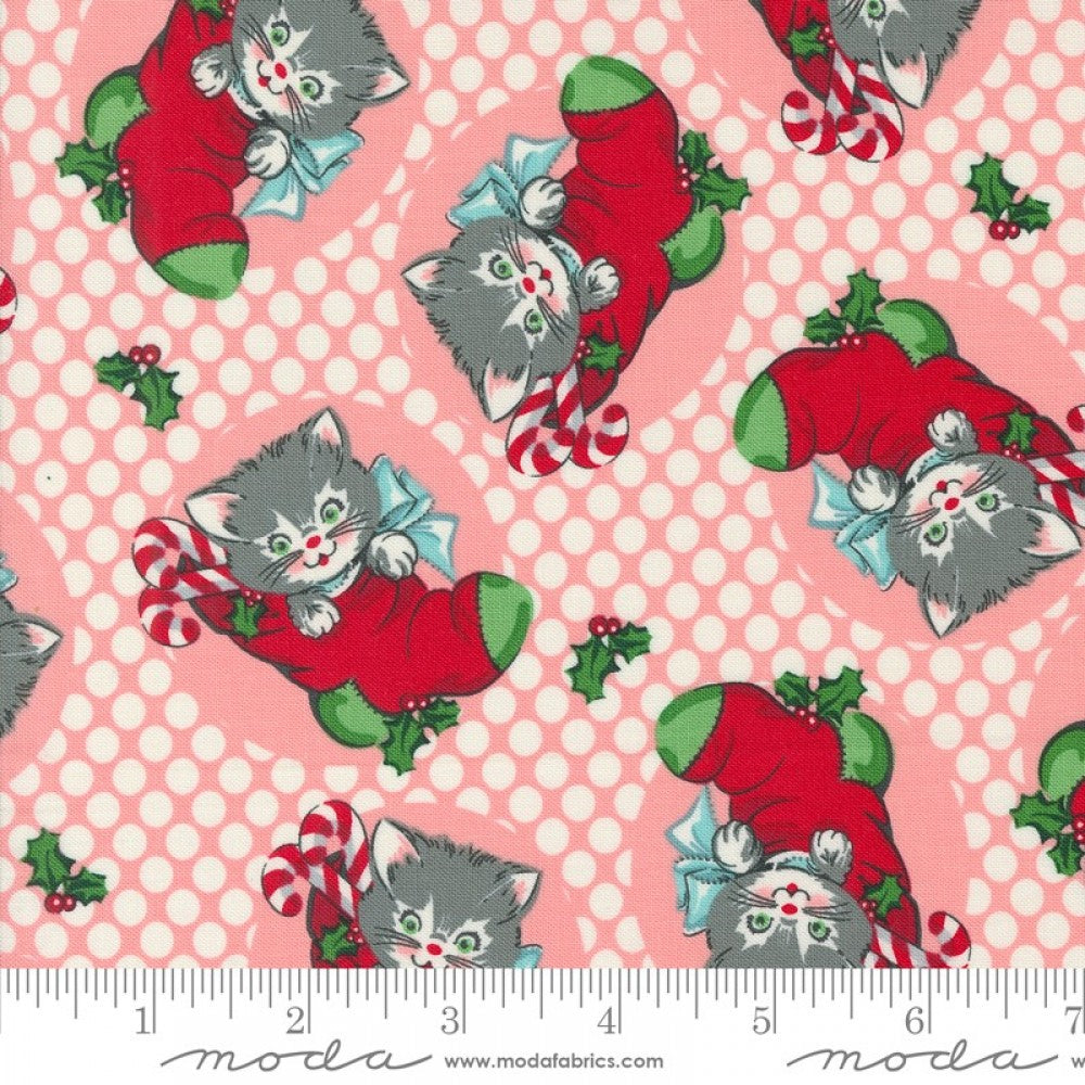 A fabric from the Kitty Christmas collection by Urban Chiks, featuring a design of cartoon kittens in red Christmas stockings on a pink background, with a ruler for scale.