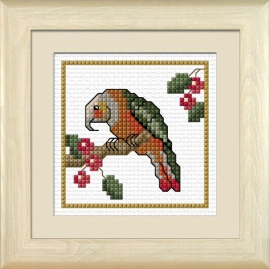 Cross-stitch kit depicting a colorful parrot with red berries on a white background, framed in a light-colored frame.