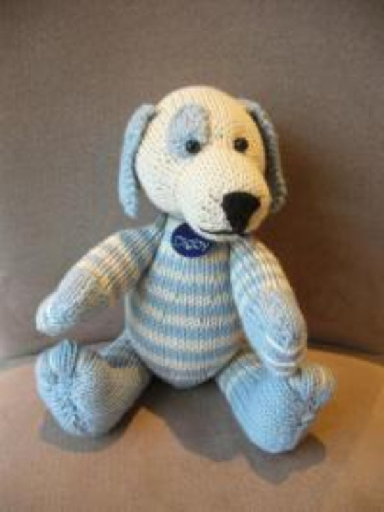 A knitted toy resembling a dog with blue and white stripes, sitting with a visible brand tag attached.