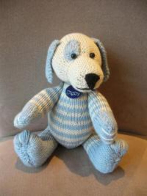 A knitted toy resembling a dog with blue and white stripes, sitting with a visible brand tag attached.
