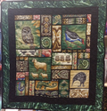 A quilt featuring various New Zealand flora and fauna designs, including birds and animals, on a green and black background.