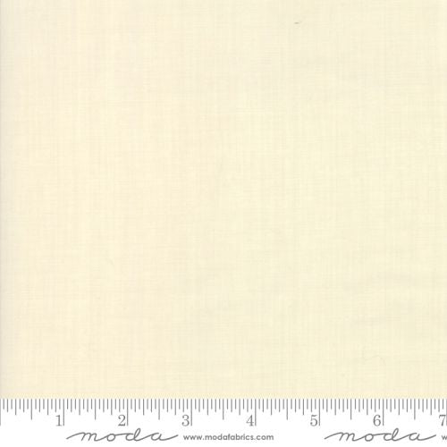 A yardstick measuring fabric; the fabric is off-white and branded with 'Moda'.
