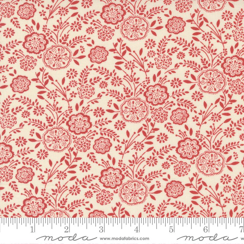 A yardstick measuring the width of a piece of Quilting fabric featuring a floral design with red flowers on a off-white background.