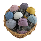 A basket containing multiple skeins of New Zealand merino yarn in various shades of blue, gray, pink, silver, and white, labeled as 'Broadway Baby Merino'.