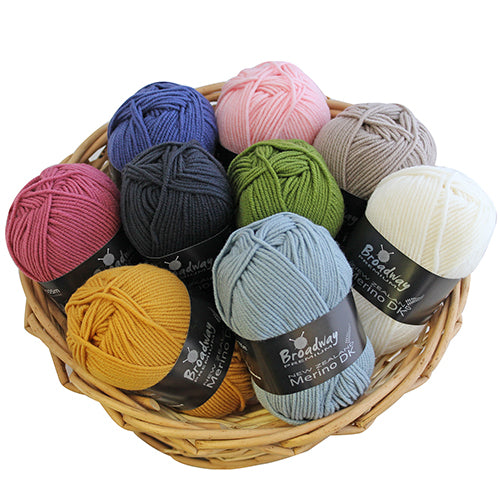 A basket containing multiple skeins of New Zealand merino yarn in various solid colors.