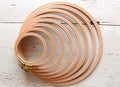 A set of wooden embroidery hoops with rounded edges and brass clasps, arranged in a circular pattern on a white wooden surface.