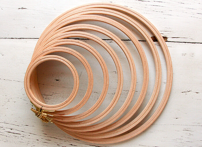 A set of wooden embroidery hoops with rounded edges and brass clasps, arranged in a circular pattern on a white wooden surface.